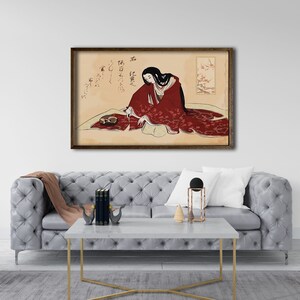 Puede incluir: Una impresi&oacute;n enmarcada de una mujer japonesa con un kimono rojo sentada en una alfombra estampada. La mujer sostiene un pincel y hay caligraf&iacute;a en el fondo. La impresi&oacute;n est&aacute; en un marco marr&oacute;n.