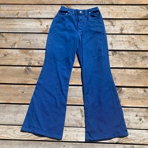 May include: A pair of high-waisted, flared-leg jeans in a solid, deep blue color. The jeans have a classic five-pocket design with a button and zipper closure. The fabric appears to be a sturdy denim, and the pants are laid flat on a wooden surface.