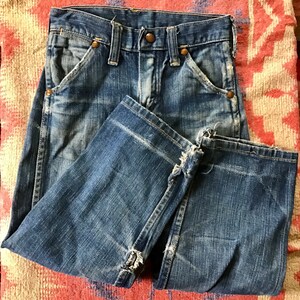 May include: Faded blue denim jeans with a classic five-pocket design. The jeans have a worn appearance with distressed details, including frayed edges and faded patches. The jeans are folded, showcasing the front pockets and button closure.