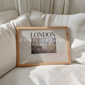 Op de afbeelding: Een houten lijst met een afbeelding van een straatbeeld in Londen. De lijst staat op een witte bank. De tekst "LONDON Frame Mockup PSD SMART OBJECT" is op de lijst gedrukt.