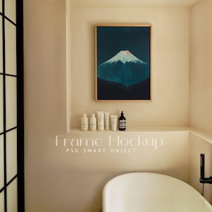 May include: A framed print of a blue mountain with a white peak against a dark blue sky hangs on a beige wall above a shelf with bottles and tubes of toiletries. The text "Frame Mockup PSD Smart Object" is printed below the shelf.
