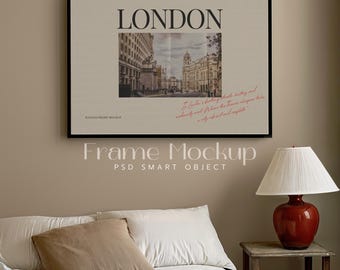 Op de afbeelding: Een zwart ingelijste poster met een foto van een straat in Londen, Engeland. De poster heeft het woord "LONDON" in grote witte letters bovenaan. De tekst "HAWKED FRAME MOCKUP" staat in de linkerbenedenhoek. De poster hangt aan een beige muur boven een bed met witte beddengoed en bruine kussens. Een lamp met een witte kap en een rode voet staat op een houten nachtkastje naast het bed.