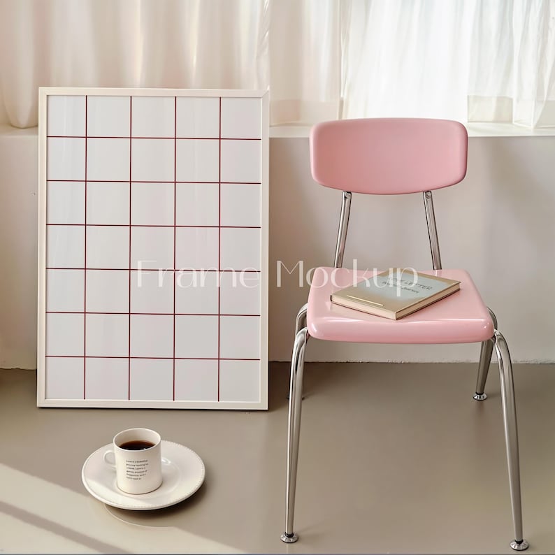 Puede incluir: Un tablero de cuadr&iacute;cula blanco enmarcado con l&iacute;neas rojas, una silla rosa con un libro en el asiento y una taza blanca con caf&eacute; en un platillo blanco.