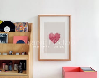 Op de afbeelding: Een ingelijst afdruk met een rood hartontwerp op een beige achtergrond. De lijst is van licht hout en de afdruk hangt aan een witte muur. De afdruk is getiteld "Frame Mockup PSD Smart Object".
