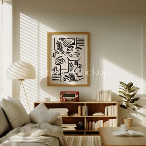 Pode incluir: Uma impress&atilde;o de arte abstrata em preto e branco em uma moldura de madeira pendurada acima de uma estante de livros de madeira cheia de livros. Um sof&aacute; branco com almofadas fica na frente da estante. Uma planta em vaso fica no ch&atilde;o ao lado da estante.