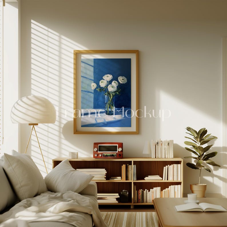 Pode incluir: Um interior de sala de estar com um sof&aacute; branco, uma estante de madeira cheia de livros, uma l&acirc;mpada e uma pintura emoldurada de flores brancas em um vaso azul sobre um fundo azul.
