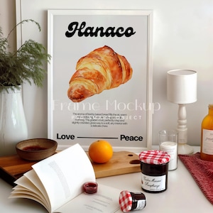 May include: A white framed poster with the word "Hanaco" in black text. The poster features a watercolor illustration of a croissant with the text "The aroma of freshly baked bread fills the air, warm and comforting.  The golden crust, perfectly crisp and slightly crackled gives way to a soft, airy interior with a delicate chew."  The poster also includes the words "Love" and "Peace".