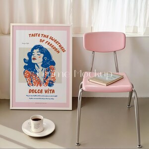 Puede incluir: Un p&oacute;ster enmarcado blanco con fondo rosa y una ilustraci&oacute;n colorida de una mujer con el texto "Taste the Sweetness of Freedom" y "Dolce Vita". Una silla rosa con un libro en el asiento y una taza de caf&eacute; en un platillo blanco est&aacute;n en primer plano.
