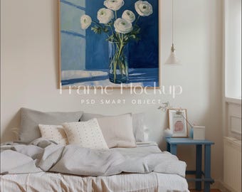 May include: A framed painting of white flowers in a glass vase against a blue background. The painting is hanging on a white wall above a bed with gray and white bedding.