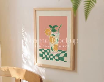May include: A framed art print featuring a refreshing drink illustration. The artwork depicts a glass of lemonade with orange slices and mint, set against a pink background and a green and white checkered pattern. The frame is light wood.