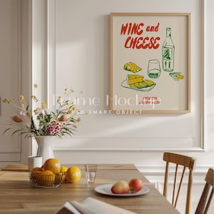 Op de afbeelding: Een ingelijste illustratie van een fles wijn, een glas wijn en een bord met kaas met de tekst "Wine and Cheese" in rode en groene letters.