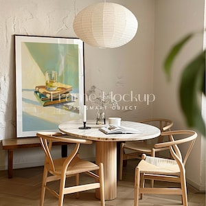 Puede incluir: Una mesa de comedor redonda de madera con una tapa de mármol blanco, rodeada de cuatro sillas de madera. Una linterna de papel blanco cuelga del techo sobre la mesa. Un cuadro enmarcado de un vaso de whisky y libros cuelga en la pared detrás de la mesa.