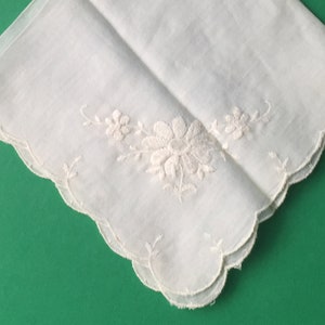 May include: White cotton handkerchief with a delicate floral embroidery design. The handkerchief has a scalloped edge.