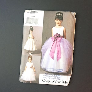 Op de afbeelding: Vogue for Me naaipatroon V7819 voor meisjesjurken. Het patroon toont illustraties van drie verschillende jurkstijlen, waaronder een witte jurk met een roze strik en een tule rok. De patroongrootte is 5, 6 en 6X.