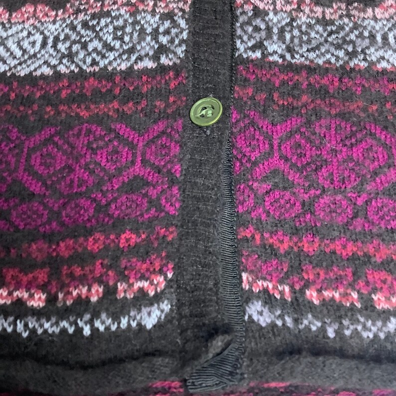 May include: Close-up of a black cardigan with a pink, white, and gray patterned design. The cardigan has a single button closure.