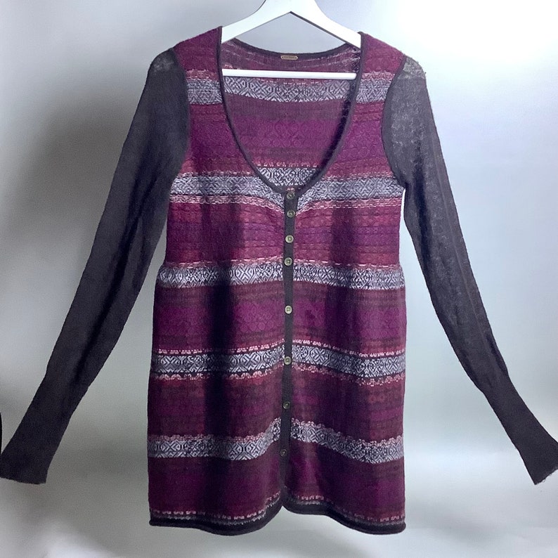 May include: A long-sleeved cardigan with a striped pattern in shades of purple, black, and white. The cardigan has a button-up front and a v-neck.