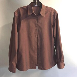 May include: A long-sleeved brown button-down shirt with a collared neckline.