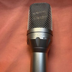 May include: A silver microphone with a mesh head. The microphone has a cylindrical body and a rounded top. The top of the microphone has a mesh screen. The microphone is designed for recording audio.