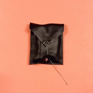 May include: A small black leather envelope with a button closure and a string attached.