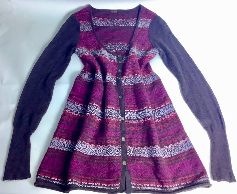 May include: A long-sleeved cardigan with a button-up front and a geometric pattern in shades of purple, pink, and brown. The cardigan has a scoop neck and a slightly flared hem.