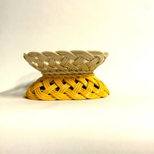May include: A woven basket with a white top and a yellow bottom. The basket is made of a woven material and has a round shape.
