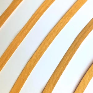 May include: Close-up of several diagonal strips of yellow fabric against a white background. The strips are evenly spaced and have a textured appearance. The fabric appears to be a woven material, possibly cotton or linen.