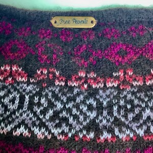 May include: A black and gray Fair Isle knit sweater with a pink and white pattern. The sweater has a metal tag that says "Free People".