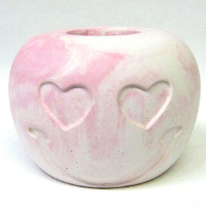 May include: A white and pink ceramic planter shaped like a heart with two hearts carved into the front.