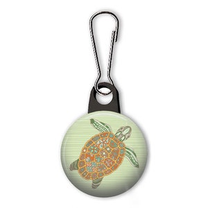 May include: A green and orange patterned turtle design on a white button with a black zipper pull. The button is attached to a black zipper pull.
