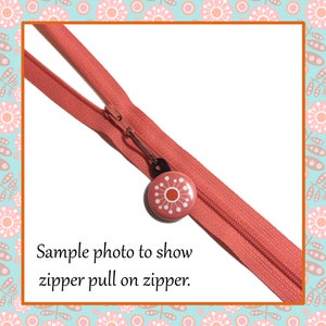 Peut inclure: Gros plan sur une fermeture &eacute;clair de couleur corail avec un tirette en forme de fleur rose et orange. La tirette est fix&eacute;e &agrave; la fermeture &eacute;clair par un anneau m&eacute;tallique argent&eacute;. Le texte "Sample photo to show zipper pull on zipper." est situ&eacute; sous la fermeture &eacute;clair.