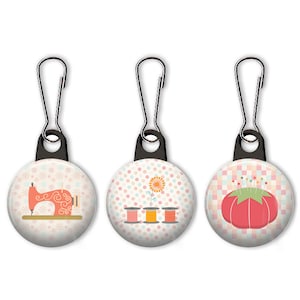 May include: Three zipper pulls with colorful sewing-themed designs. The first pull features a red sewing machine on a pink and white snowflake background. The second pull has three spools of thread and a flower on a pink and white polka dot background. The third pull has a red pincushion with pins on a pink and white checkered background.