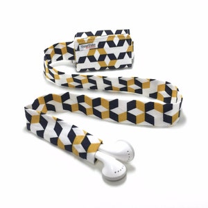 May include: A white, black, and yellow geometric patterned fabric headphone strap with a small fabric pouch that says "TuneTube" and white earbuds.