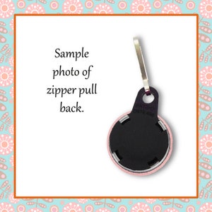 May include: Back view of a pink zipper pull with a black round disc and a silver metal loop. The disc has the word "PATENT" and a number printed on it.