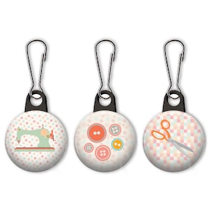 May include: Three zipper pulls with colourful, patterned buttons, sewing machine, and scissors designs. The buttons are pink, orange, and yellow. The sewing machine is green and white. The scissors are orange and silver.