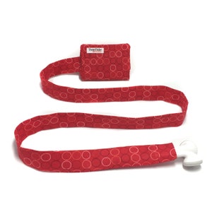 May include: Red fabric lanyard with a white plastic clip and a small red fabric pouch with the text "TuneTube" printed on it. The pouch and lanyard have a white circle pattern.