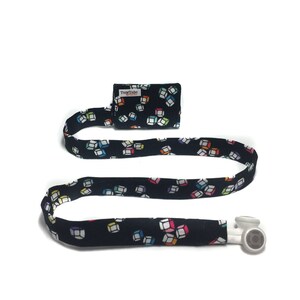 May include: A black fabric lanyard with a colorful cube pattern. The lanyard has a small black fabric pouch with the text "TuggTube" on it. The lanyard has a white headphone jack at the end.