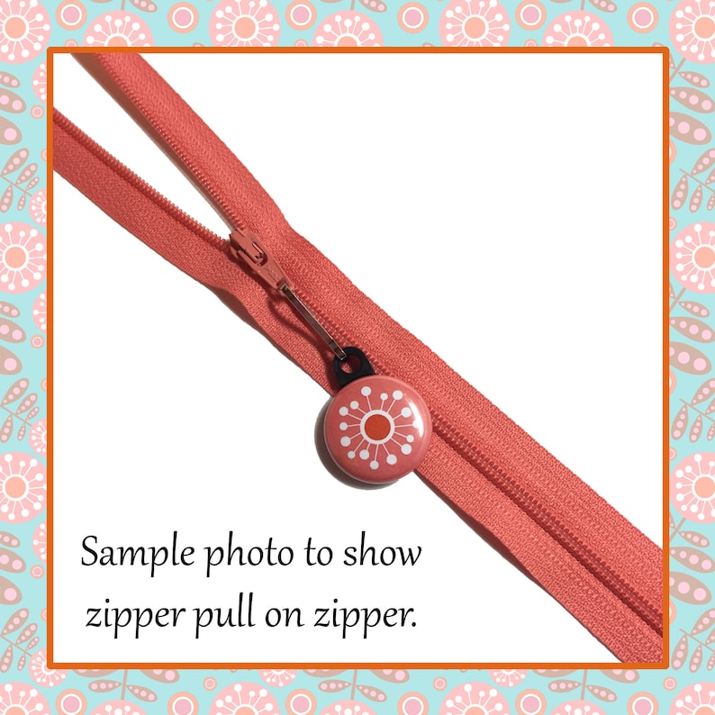 May include: A close-up of a coral pink zipper with a coral pink button zipper pull featuring a white stylized flower design. The text "Sample photo to show zipper pull on zipper." is below the zipper.