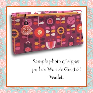 Peut inclure: Gros plan sur un tirette de fermeture &eacute;clair sur un portefeuille &agrave; motif floral rose et rouge. La tirette de fermeture &eacute;clair est un petit bouton rond rouge avec un motif blanc. Le texte "World's Greatest Wallet" est visible sous l'image.