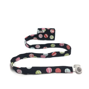 May include: A black and white polka dot lanyard with a small black pouch that says "TummyTube" on it. The lanyard has a white plastic clip on one end.