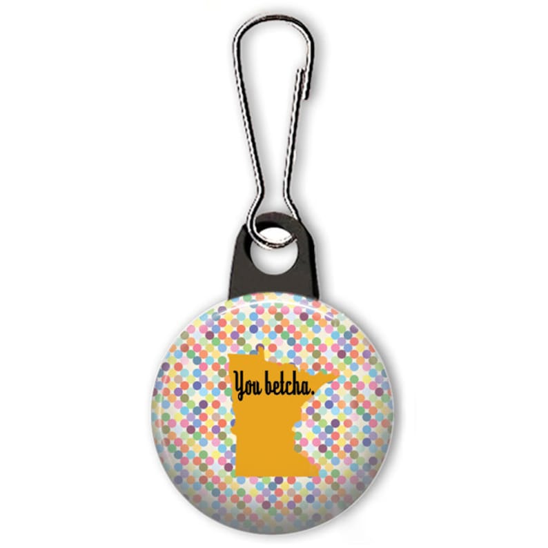 May include: A colorful polka dot button with a yellow outline of the state of Minnesota and the text "You betcha." The button is attached to a black zipper pull.