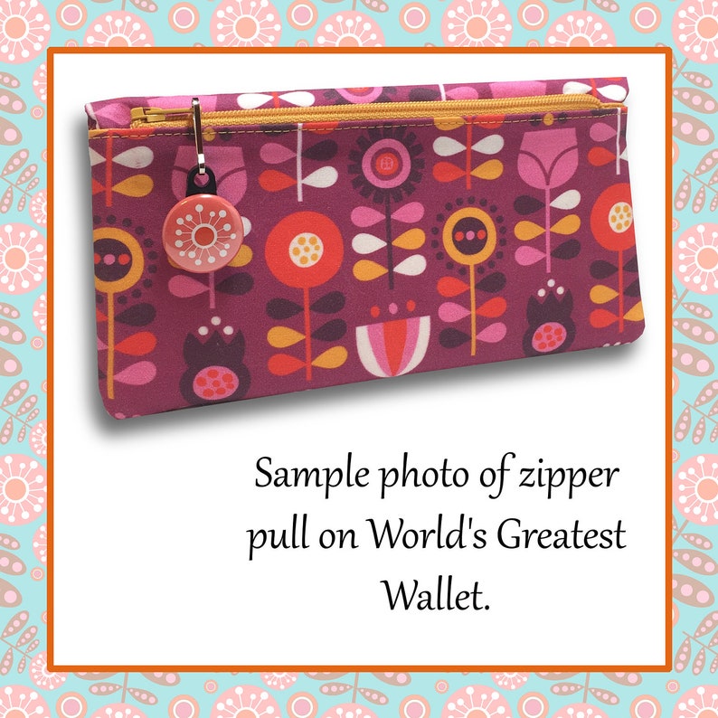 May include: A close-up of a zipper pull on a pink and red floral patterned wallet. The zipper pull is a small, round, red button with a white design. The text "World's Greatest Wallet" is visible below the image.