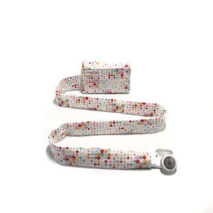 May include: A white lanyard with a colorful polka dot pattern. The lanyard has a small white pouch with the text "TuneTube" on it. The lanyard has a white earbud attached to the end.