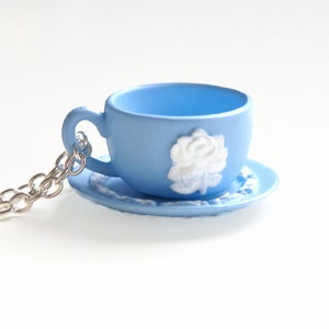 May include: A light blue teacup and saucer necklace with a white rose design. The necklace is made of a silver chain.
