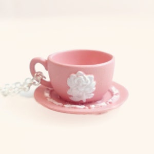 May include: A pink teacup and saucer necklace with a white rose design. The necklace is made of silver chain.
