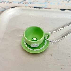 May include: A green teacup and saucer necklace with a green gem in the centre of the teacup.