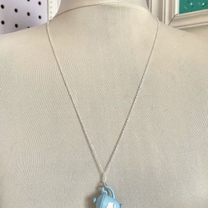 May include: A silver chain necklace with a light blue teapot pendant. The teapot has a white floral design.