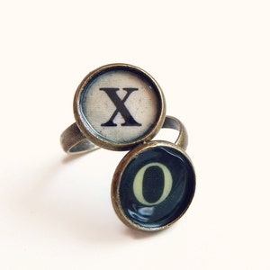 May include: A ring with two typewriter keys, one with the letter 'X' and the other with the letter 'O'. The keys are set in bronze-colored metal.