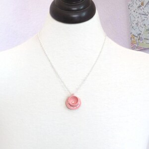 May include: A delicate silver chain necklace with a pink teacup pendant. The teacup has a white rim and a small pearl in the centre.