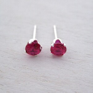 Puede incluir: Un par de pendientes de botón de plata con pequeñas piedras redondas de color rosa brillante.