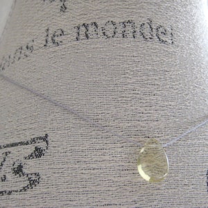 Puede incluir: Un collar sencillo con un colgante transparente en forma de l&aacute;grima. El colgante est&aacute; hecho de un material amarillo claro.